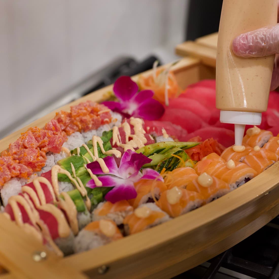 Finishing specialty rolls on a sushi boat with sauce and orchids.
