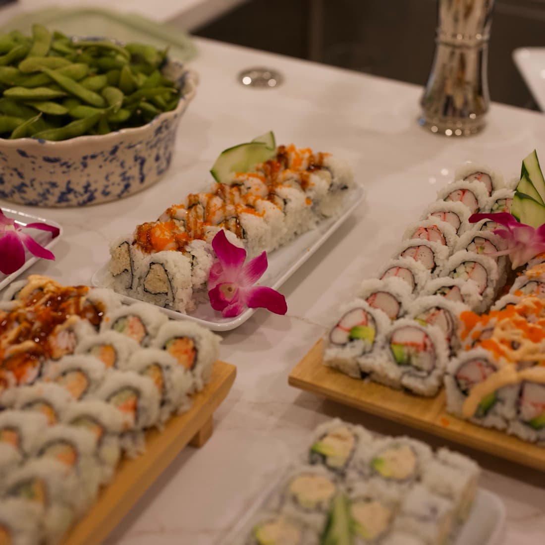 Platters of specialty rolls and edamame laid out on the kitchen counter.
